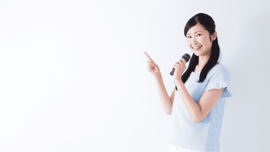 マイクを持って指を指す女性