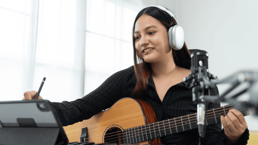 ヘッドフォンをしてギターを持ちながらメモをする女性
